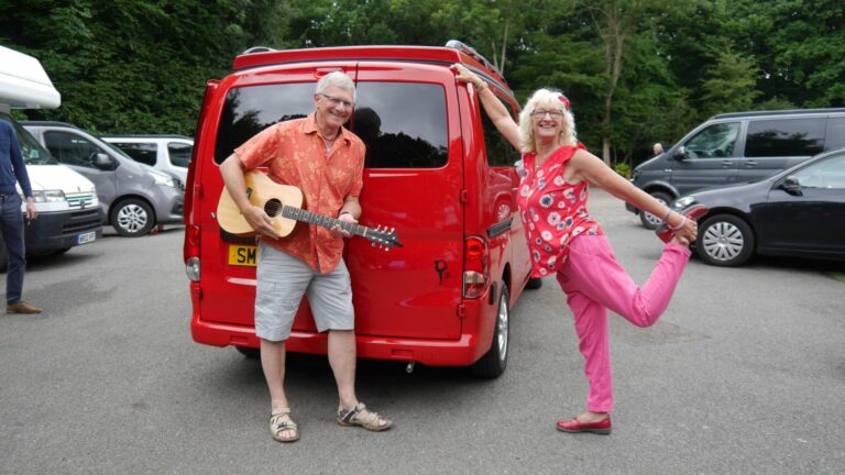 husband and wife happily standing at the back of their campervan